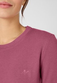 Maglione a costine viola con scollo rotondo e piccolo logo ricamato sulla parte sinistra del petto. Texture morbida, silhouette aderente.