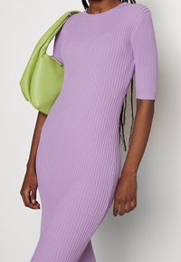 Robe en lilas côtelée avec manches courtes, coupe près du corps et tissu texturé. Associée à un sac hobo vert vif.