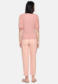 Pink puff sleeve top paired with light pink, tailored trousers. The top features a textured finish; trousers have rolled cuffs. Flat shoes complete the look.