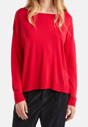 Punainen neulepaita, jossa leveä venepääntie, lörpähtävät olkapäät ja resorit hihansuissa. Yhdistetty tummiin teksturoituihin housuihin.