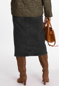 Dunkelblaue Denim-Midirock mit geradem Schnitt, kombiniert mit kniehohen braunen Wildleder-Stiefeln mit Absatz. Olivgrüne gesteppte Jacke und braune Handtasche.