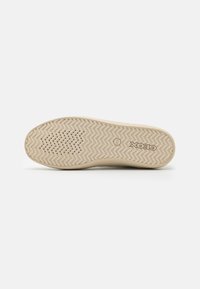 Suela de deporte beige con un patrón de banda de rodadura en zigzag y pequeños orificios de ventilación. Logo en la zona del talón, material de goma lisa.