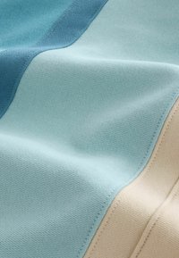 Gros plan de sections de tissu doux en bleu clair, sarcelle et beige avec des coutures visibles et une texture lisse.