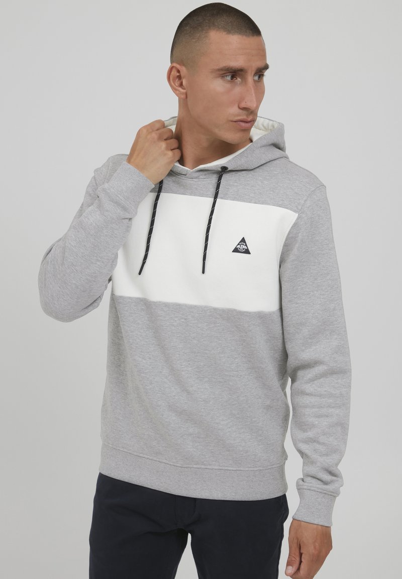 Grijze hoodie met een witte horizontale strook en zwarte trekkoorden. Bevat een klein zwart driehoeklogo op de borst. Zachte katoenconstituentie.