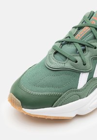 Green sneaker featuring mixed materials of textile and leather, with a textured surface, white accents, and a gum rubber sole.