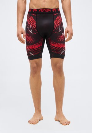 Black and red compression shorts with snake scale pattern worn by a standing shirtless person against a plain background.