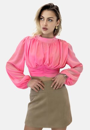 Rosa durchsichtige Bluse mit Puffärmeln und gerafften Details, kombiniert mit einem figurbetonten beigen Minirock. Glatte Texturen und lebendiger Farbkontrast.