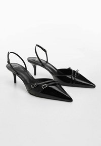 Talons aiguilles en cuir verni noir avec bout pointu et talons fins. Présente de petites boucles et des sangles croisées pour un détail supplémentaire.