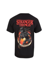 Černé bavlněné tričko s grafickým potiskem postavy ze "Stranger Things" s červeným textem nahoře a podrobnou ilustrací níže.