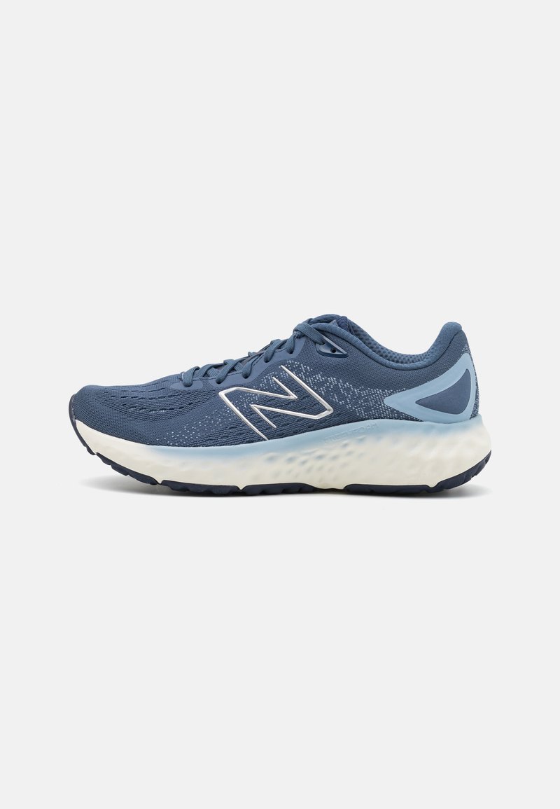 Zapatilla de running azul con parte superior de malla texturizada, logo N blanco, acentos azul claro y una mediasuela acolchada de color blanco con manchas. Suela de goma.