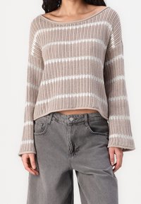 Beige Strickpullover mit weißen horizontalen Streifen, ausgestattet mit einem weiten Boots-Ausschnitt und Glockenärmeln. Kombiniert mit grauen Jeans in lässiger Passform.