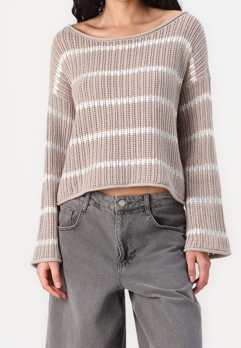Beige Strickpullover mit weißen horizontalen Streifen, ausgestattet mit einem weiten Boots-Ausschnitt und Glockenärmeln. Kombiniert mit grauen Jeans in lässiger Passform.