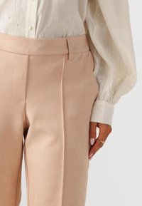 Lichtroze op maat gemaakte broek met een gladde textuur, voorzien van een vlak voorkant en steekzakken in de zijnaad, gecombineerd met een witte blouse versierd met borduurwerk.