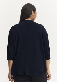 Granatowy sweter z dzianiny z rękawami o długości trzech czwartych, luźny krój, subtelne detale szwów z tyłu oraz zaokrąglony dół. Gładka tekstura.