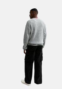 Grå stickad tröja med lös passform, kombinerad med svarta cargobyxor med flera fickor och vita sneakers. Bakvy.