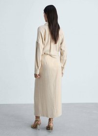 Beige lange mouw jurk, knie-lengte met een rechte pasvorm en een kraag. Voorzien van een gladde textuur met een subtiele glans, gedragen met tan kleurige hakken sandalen.