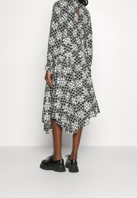 Šaty s černobílým vzorem, dlouhými rukávy, vysokým výstřihem a vrstveným lemem. Nosit s černými šněrovacími botami.