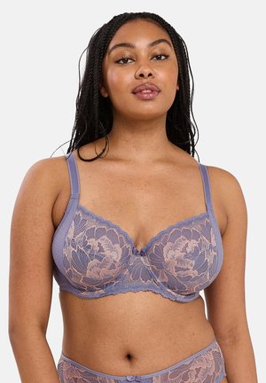 Mujer modelando sujetador de encaje púrpura y ropa interior a juego con patrón floral, mirando hacia adelante sobre fondo liso.