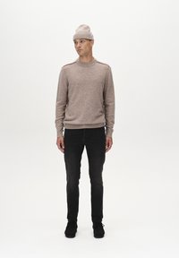 Beiger Strickpullover mit Rundhalsausschnitt, strukturierter Stoff, gerippte Bündchen, kombiniert mit schwarzen Slim-Fit-Jeans und schwarzen Schuhen, getragen mit einer passenden Mütze.
