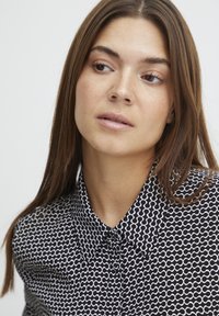 Camicia a fantasia bianco e nero con colletto, chiusura a bottoni e un motivo a onde ripetuto su un tessuto liscio.