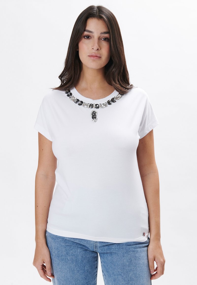 Camiseta blanca de manga corta con un cuello decorativo en negro y plata. Tejido suave con una forma ajustada.