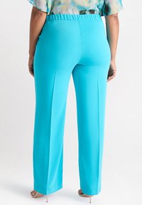 Aqua blauwe, wijde broek met een soepele textuur en een elastische tailleband. Heeft strakke lijnen en een getailleerde pasvorm bij de enkels.
