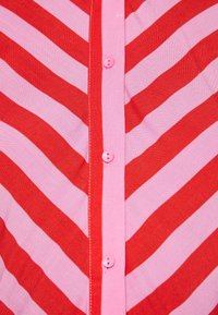 Tessuto a righe chevron rosso e rosa con una chiusura frontale a bottoni caratterizzata da bottoni rosa e cuciture a contrasto lungo la patta.