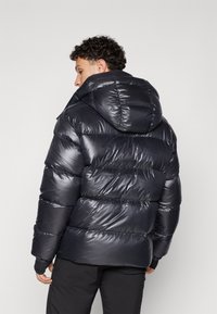 Must must jacket läikiva, tikitud pinnaga ja suure kapuutsiga. Omab horisontaalseid paneele ja elastseid mansette soojuse ja mugavuse tagamiseks.