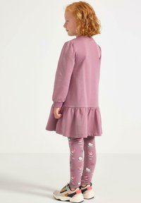 Rosa långärmad klänning med volangkant, kombinerad med mönstrade leggings med Hello Kitty. Skorna har en kraftig sula med flerfärgade accenter.