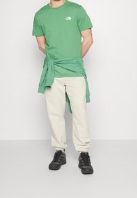 Green cotton t-shirt with crew neckline, paired with cream-colored pants and black hiking shoes, featuring a green sweatshirt tied at the waist.