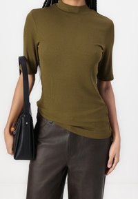 Oliwkowy, prążkowany t-shirt z krótkim rękawem i wysokim dekoltem, zestawiony z ciemnobrązowymi spodniami skórzanymi i czarną torebką.
