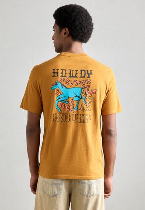 Kortermet sennepsgul T-skjorte med et blått grafisk motiv av en hest og tekst på baksiden. Laget av myk bomull med en avslappet passform.