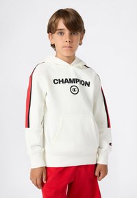 Witte hoodie met zwarte "CHAMPION" logo, rode en zwarte strepen langs de mouwen, voorzak en gestructureerde stof.