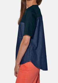 Top in misto denim e cotone caratterizzato da una sezione superiore blu navy con maniche corte, una tasca e un orlo curvo, abbinato a pantaloni corallo.