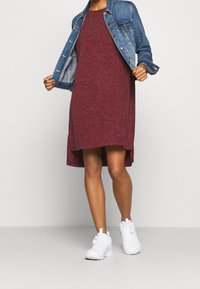 Vínová krátkosrstá šaty s vysokým a nízkým lemem, spárované s denimovou bundou. Bílé sportovní tenisky doplňují celý outfit.