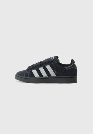 Czarny sneaker Adidas Campus z białymi paskami, czarnymi sznurowadłami i gumową podeszwą, widoczny z boku na jasnym, jednolitym tle.