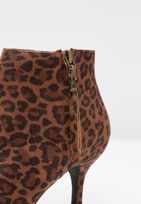 Stivale alla caviglia con stampa leopardata realizzato in camoscio marrone. Presenta una zip laterale con dettagli in ottone e un design con tacco alto. Texture liscia.