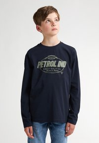 Marineblaues langärmliges T-Shirt aus Baumwolle mit einem großen grünen Logo auf der Vorderseite. Kombiniere es mit hellblauen Jeans.