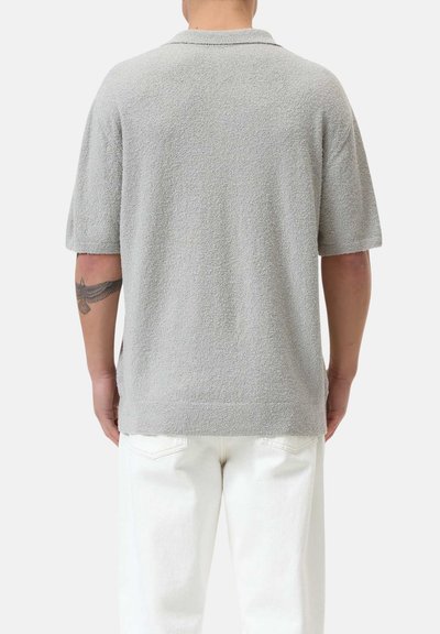 Polo shirt grigio a maniche corte in tessuto texturizzato, con colletto e vestibilità comoda, abbinato a jeans bianchi.