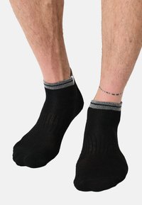 Calzini neri alla caviglia con tessuto strutturato e polsini grigi a coste. I calzini sono aderenti e hanno una finitura liscia.