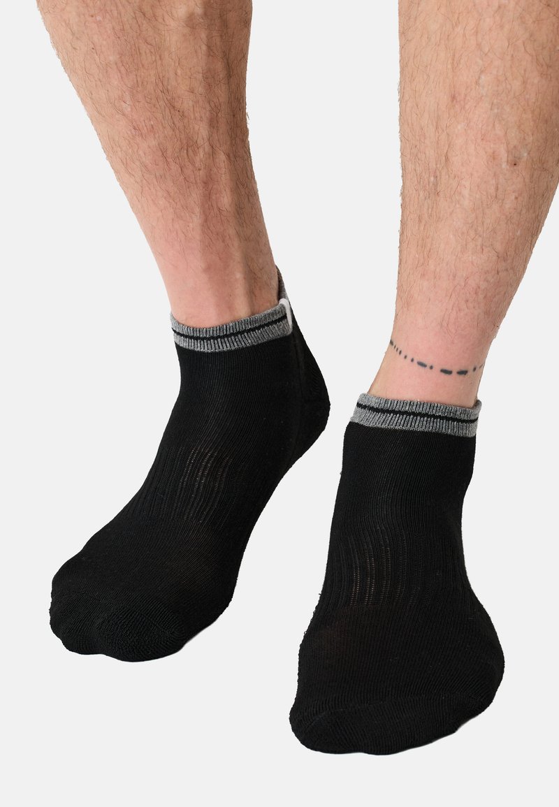 Calzini neri alla caviglia con tessuto strutturato e polsini grigi a coste. I calzini sono aderenti e hanno una finitura liscia.