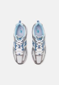 Un paio di scarpe da corsa New Balance bianche e argento con accenti blu e lacci bianchi, viste dall'alto su uno sfondo bianco.
