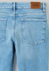 Jean en denim bleu clair avec une texture lisse, comportant deux poches arrière et une étiquette en cuir marron sur la ceinture marquée "BZF."
