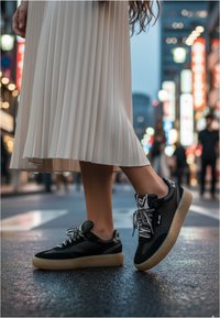 Czarne sneakersy z teksturowanej skóry i perforowanymi akcentami, z jasnobrązową gumową podeszwą i szarymi sznurówkami, zestawione z plisowaną beżową spódnicą.