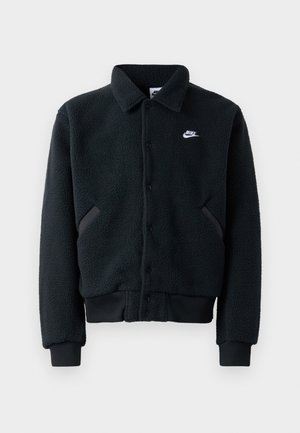 Schwarze Fleecejacke mit Knopfverschluss, gerippten Bündchen und Saum. Mit einem kleinen weißen Nike-Logo auf der linken Brust und seitlichen Taschen.