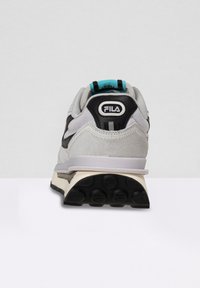 Sneaker grigia e nera con tomaia in suede e mesh, caratterizzata da accenti turchesi e una suola in gomma con pattern di battistrada circolari.