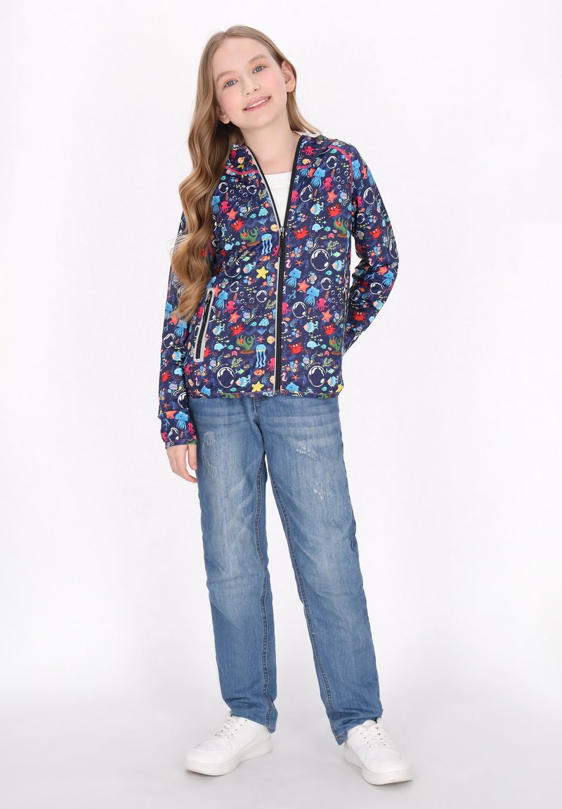 Marineblå zip-up jakke med farverige havdyrmønstre, parret med lyseblå jeans og hvide sneakers.