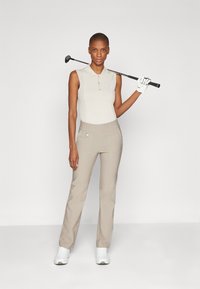 Tenue de golf comprenant un polo sans manches beige et un pantalon droit beige, avec un club de golf et des baskets blanches. Texture lisse, design ajusté.