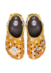Yellow clogs featuring a triangular pattern, black holes, and decorative accents including a bird and text patches. Adjustable strap included.