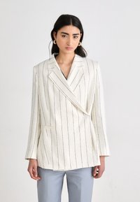 Blazer blanco con rayas verticales azules, diseño de doble botonadura, solapas con muesca y bolsillo frontal. Tejido suave, corte entallado.